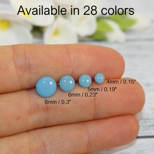 Può includere: Quattro orecchini a lobo azzurri di diverse dimensioni, da 4 mm a 8 mm (0,15" a 0,3"). Il testo "Disponibile in 28 colori" è visibile nella parte superiore dell'immagine.