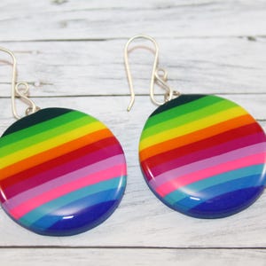 Könnte beinhalten: Ein Paar runde Ohrringe mit Regenbogenstreifen. Die Ohrringe haben einen silbernen Haken und bestehen aus glänzendem Material. Die Farben sind Grün, Gelb, Rot, Rosa und Blau.