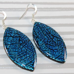 Peut inclure: Une paire de boucles d'oreilles pendantes avec des pendentifs en forme de marquise arborant un motif craquelé bleu vif et noir. Les pendentifs sont suspendus à des crochets en métal argenté, créant un contraste net entre la base sombre et la finition bleue.