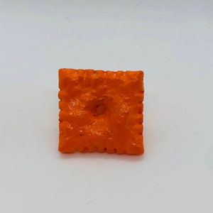 May include: Orange square-shaped cracker with a hole in the center.