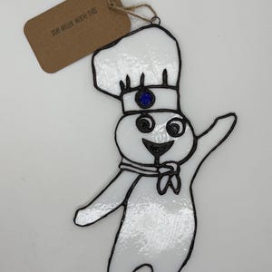 May include: Stained glass ornament featuring a smiling chef character in a white chef's hat and uniform, outlined in black. The chef has a blue gem on the hat. A tag reads "SUB MILLER MADE THIS".