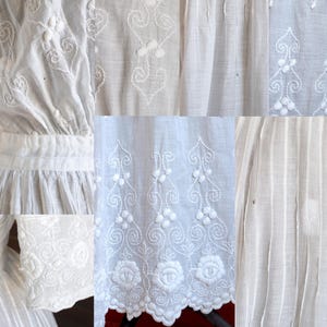 May include: Close-up of a white dress with intricate embroidered details. The dress features floral and scrollwork patterns, with a scalloped hemline. The fabric appears to be lightweight and textured, with vertical pleats and detailed sleeves.