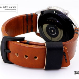 May include: A brown leather watch band with black stitching and a black buckle. The band is double-sided, meaning it has the same smooth finish on both sides. The band is shown attached to a silver smartwatch.