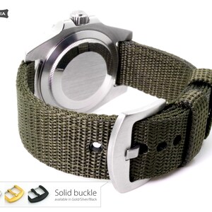 May include: A green nylon watch strap with a silver buckle. The strap is attached to a silver watch with a black face. The text "Solid buckle" is visible below the watch. The text "available in Gold/Silver/Black" is visible below the text "Solid buckle".