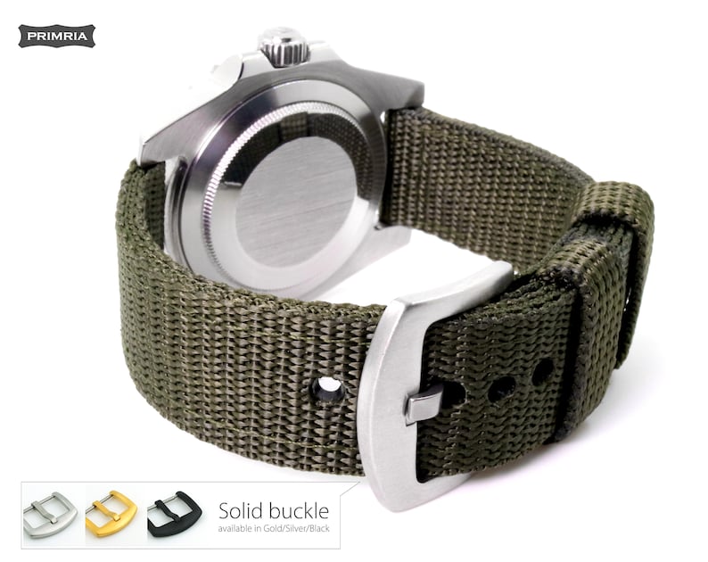 May include: A green nylon watch strap with a silver buckle. The strap is attached to a silver watch with a black face. The text "Solid buckle" is visible below the watch. The text "available in Gold/Silver/Black" is visible below the text "Solid buckle".