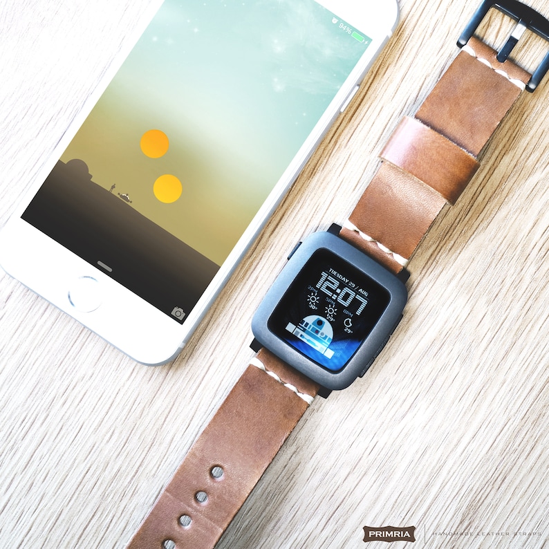 K&ouml;nnte beinhalten: Ein braunes Lederarmband mit einem schwarzen Smartwatch-Zifferblatt, das die Zeit 12:07 und das Datum Donnerstag, 27. August anzeigt. Das Zifferblatt zeigt auch ein Wettersymbol und eine Temperatur von 25 Grad an. Die Smartwatch liegt auf einer Holzoberfl&auml;che neben einem wei&szlig;en iPhone mit einem Star Wars-Hintergrundbild.