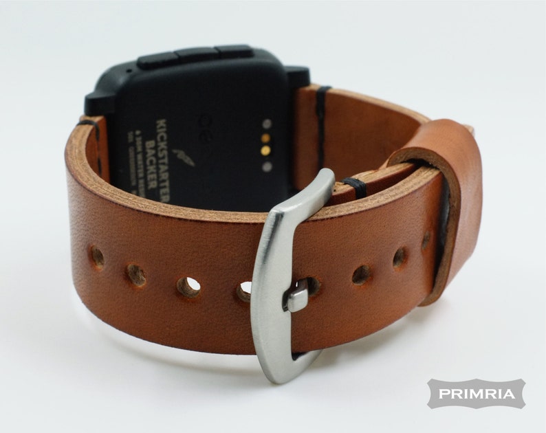 K&ouml;nnte beinhalten: Ein braunes Lederarmband mit einer silbernen Schlie&szlig;e. Das Armband ist f&uuml;r eine Smartwatch mit schwarzem Zifferblatt und vier Kn&ouml;pfen konzipiert. Der Text "Kickstarter Backer" ist auf dem Zifferblatt der Uhr sichtbar.