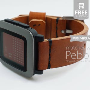 K&ouml;nnte beinhalten: Ein braunes Lederarmband mit schwarzen N&auml;hten, das f&uuml;r eine Pebble Smartwatch konzipiert ist. Das Armband ist an einer Pebble Smartwatch mit einem grauen Metallgeh&auml;use und einem schwarzen Bildschirm, auf dem ein Kalender angezeigt wird, befestigt.