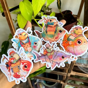 May include: A collection of colorful fish stickers, each adorned with unique outfits and accessories. The stickers feature a variety of fish species in shades of blue, orange, red, and purple, with detailed illustrations and whimsical designs.