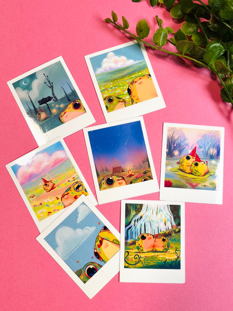 May include: Set of 7 illustrated Polaroid-style cards featuring cartoon frogs in various settings. The frogs are green with yellow spots and have large eyes. The settings include a forest, a field of flowers, a campfire, a waterfall, and a night sky with a shooting star.