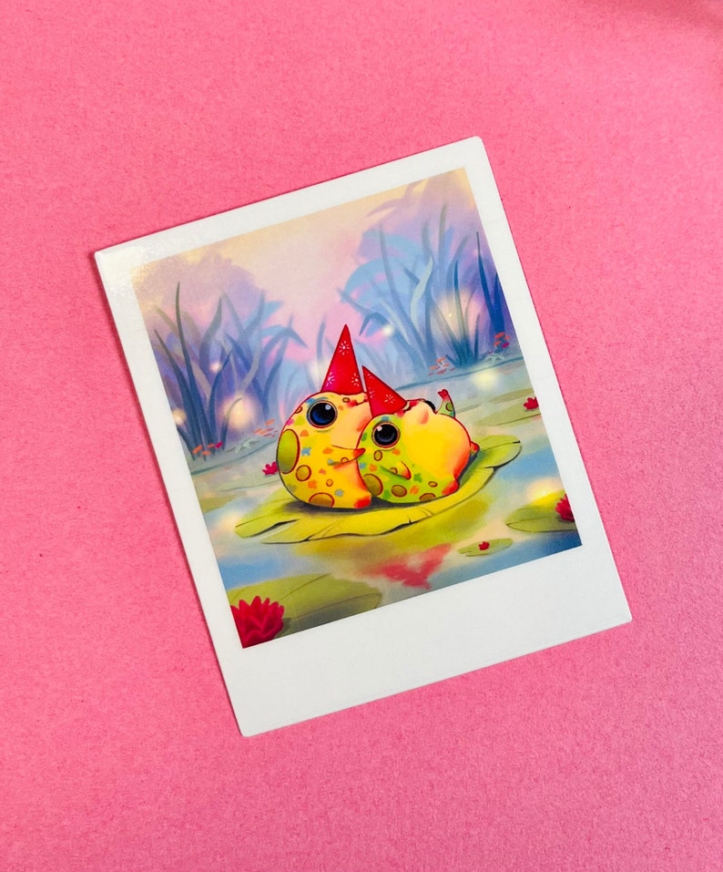 May include: Two yellow and green frogs wearing red party hats sit on a lily pad in a pond. The pond is surrounded by tall grass and the background is a soft blue and purple.