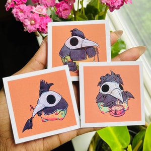 May include: Three square stickers with illustrations of plague doctor masks and crows on an orange background. The masks are white with black eye holes and beaks. The crows are black. One sticker has a crow holding a small red object.