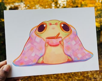 May include: A cute cartoon creature with big eyes is wrapped in a pink and purple blanket and holding a bowl of soup. The creature has a yellow body and a green head.