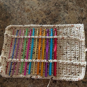 May include: A set of 16 colorful crochet hooks organized in a crocheted holder. The hooks are arranged in a rainbow pattern and are made of metal.