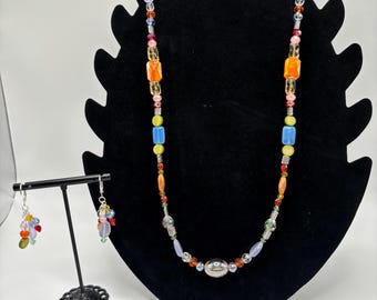 May include: A colorful beaded necklace with a silver oval pendant and matching earrings. The necklace features a variety of colors, including blue, green, yellow, orange, and red.