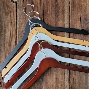 May include: Four wooden hangers in different colors: black, brown, beige, and white. The hangers are stacked on top of each other, with the black hanger on top.
