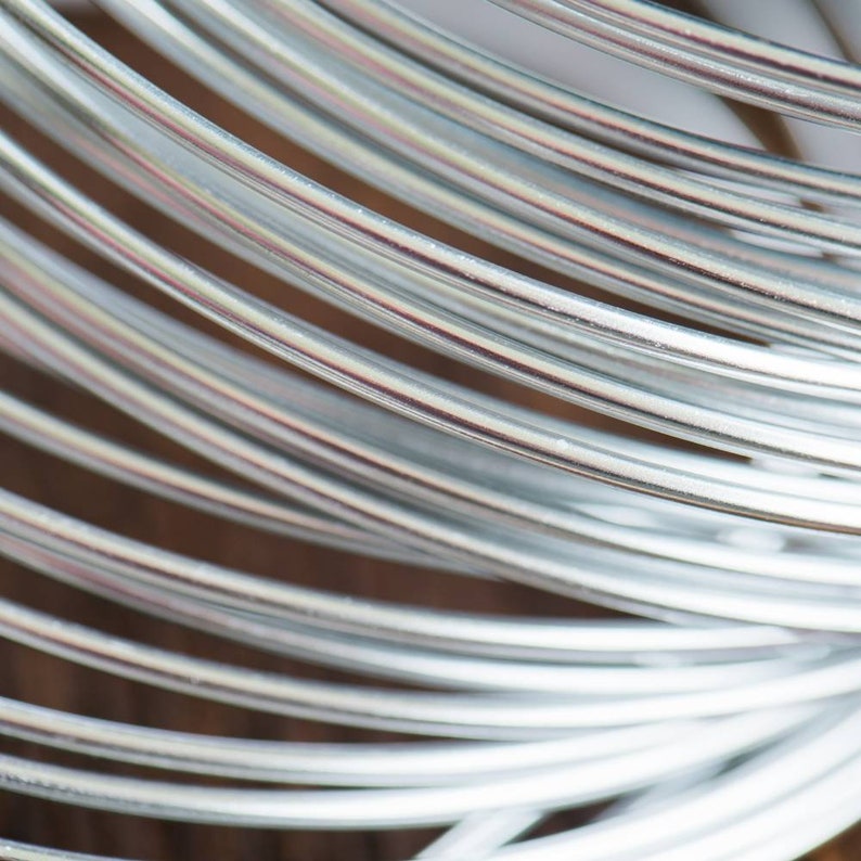 May include: Close-up of a coil of silver-colored wire. The wire is smooth and shiny, and it is wound tightly together.