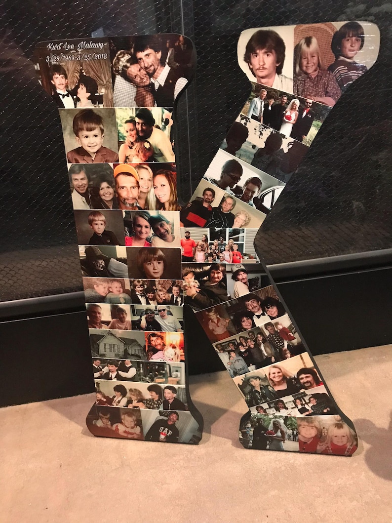 May include: A large wooden letter "K" decorated with numerous photographs. The photos are of various sizes and feature people of different ages and settings. The letter is black with a dark brown border and sits on a light-colored surface.