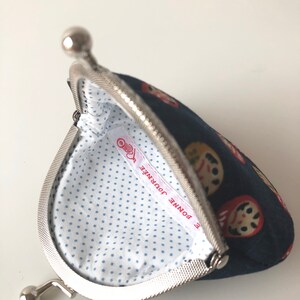 May include: A blue fabric coin purse with a silver clasp. The purse is decorated with a pattern of Japanese dolls. The inside of the purse is lined with white fabric with blue polka dots. The label inside the purse reads "Bonne Journee".