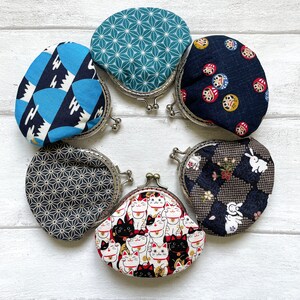 May include: Six different coin purses with various Japanese-inspired patterns. The purses are made of fabric and have metal frames. The patterns include a blue and white geometric design, a green and white geometric design, a black and white geometric design, a black and white floral design, a black and white cat design, and a blue and white design with red and gold accents.
