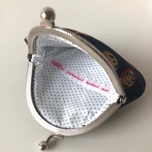 May include: A blue coin purse with a white polka dot lining. The purse has a silver clasp and a silver loop handle. The lining has a red and white label that says "UNE BONNE JOURNEE".