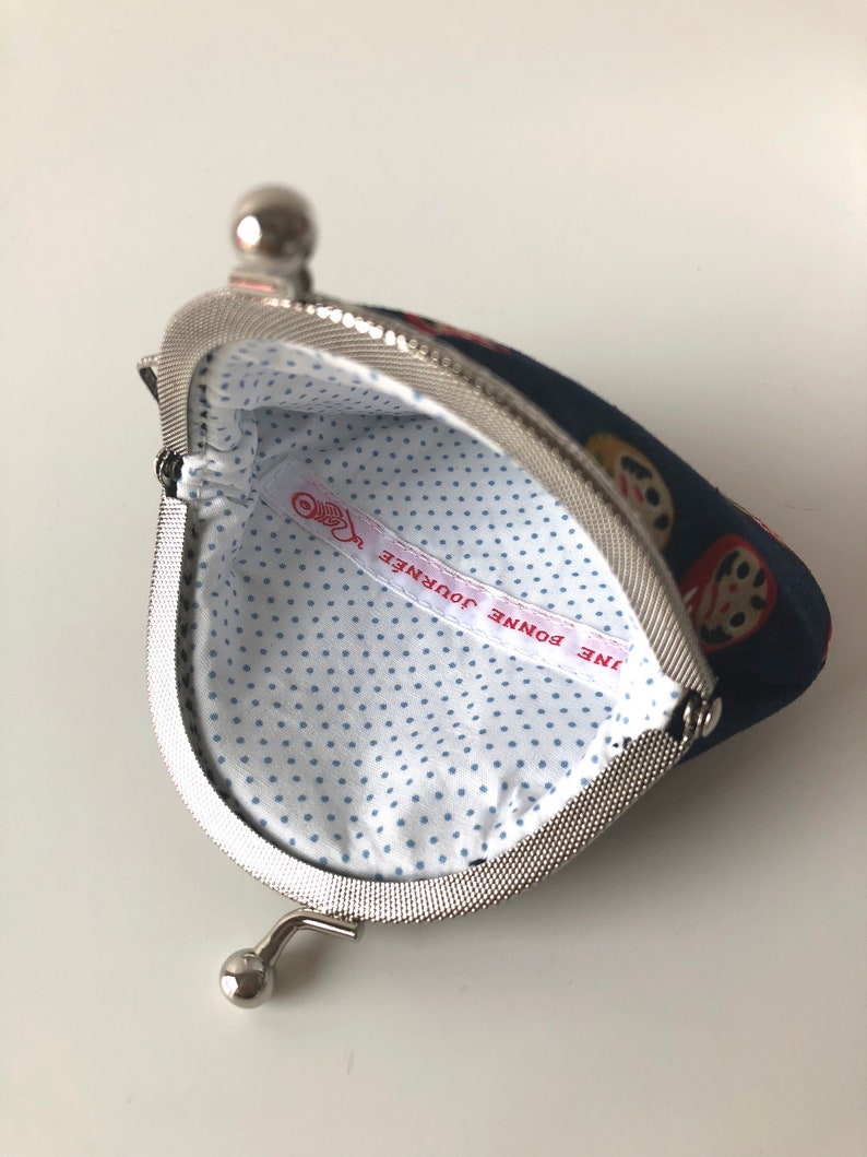 May include: A blue coin purse with a white polka dot lining. The purse has a silver clasp and a silver loop handle. The lining has a red and white label that says "UNE BONNE JOURNEE".