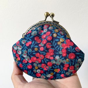 Peut inclure: Une petite bourse à monnaie bleue avec un motif floral composé de fleurs rouges, jaunes et vertes. La bourse a un fermoir en laiton.