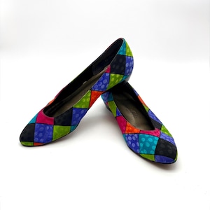 May include: A pair of colorful, patterned flats. The shoes feature a patchwork design with squares of black, blue, green, pink, and orange, accented with polka dots. The shoes have a pointed toe and a low heel.