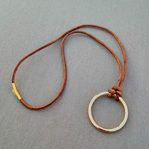May include: A brown leather necklace with a gold-colored circular pendant. The necklace has a simple design with a knotted closure and a gold-colored clasp. The pendant is a large, open circle.