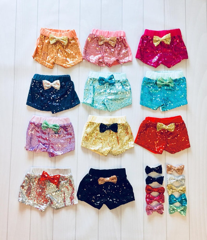 May include: Ten pairs of sequined shorts for girls, each with a different color and bow. The colors include pink, red, blue, green, gold, silver, and black.