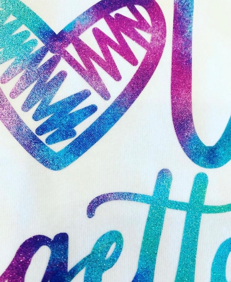 K&ouml;nnte beinhalten: Ein wei&szlig;es T-Shirt mit einem glitzernden blau-violetten Herzen und dem Wort "gotta" in glitzerndem Blau und Lila.