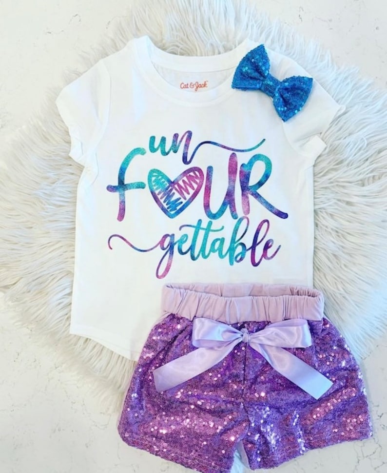 K&ouml;nnte beinhalten: Ein wei&szlig;es T-Shirt mit einer regenbogenfarbenen Grafik, auf der "fun four gettable" mit einem Herzen in der Mitte des Wortes "four" steht. Das Shirt wird mit einem lilafarbenen Pailletten-Shorts mit einer lavendelfarbenen Schleife kombiniert.