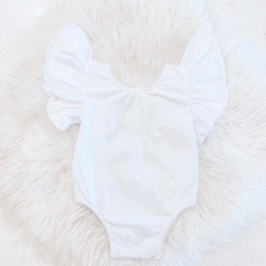 May include: White baby onesie with ruffled sleeves. The onesie is made of a soft, stretchy fabric and has a scoop neckline.