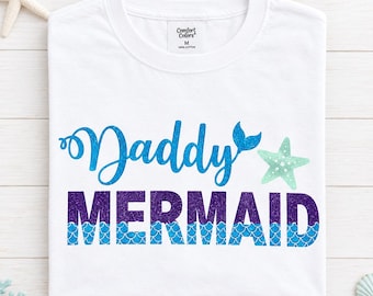 May include: A white t-shirt featuring the blue glittery text Daddy with a small mermaid tail accent, followed by the word MERMAID in purple glittery text with a blue scale pattern at the bottom and a light green starfish graphic to the right.