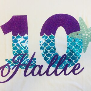 May include: Purple glitter number 10 with teal mermaid scales and a teal glitter starfish. The name "Hallie" is written in purple glitter below the number.