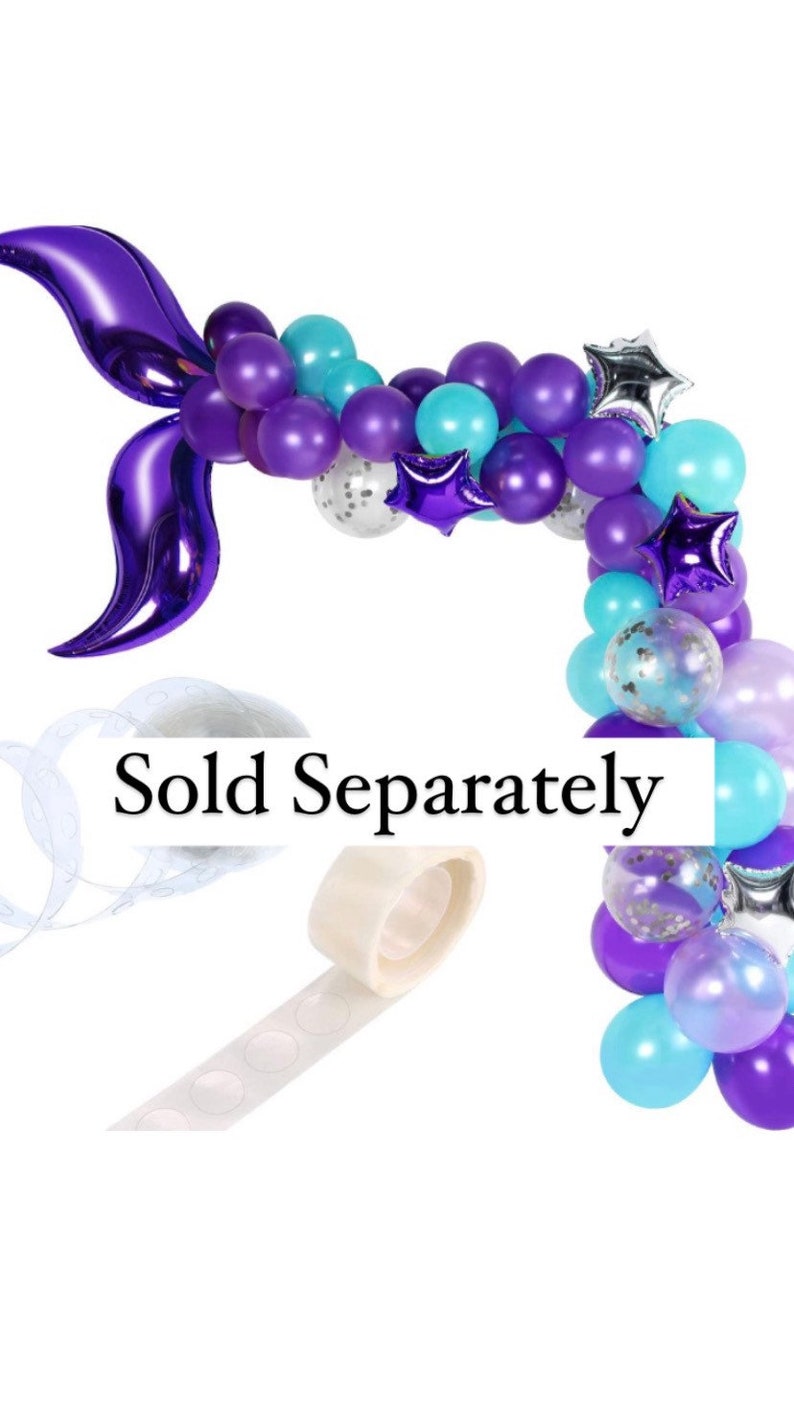 May include: A purple and blue balloon garland with a purple foil mermaid tail. The garland is decorated with silver and purple stars. The text "Sold Separately" is visible in the image.