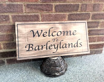 May include: A wooden sign saying "Welcome to Barleylands" in black script. The sign has a dark border and is supported by a woven basket. The background is a red brick wall.