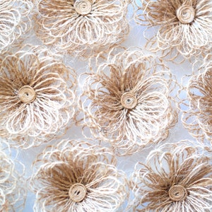 May include: A collection of brown and white burlap flowers with a delicate, woven texture. The flowers are arranged in a circular pattern on a white background.