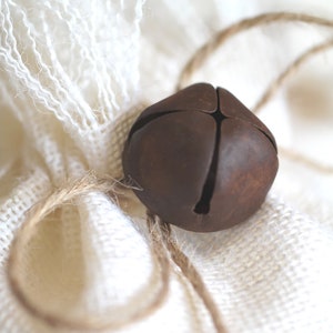 May include: A rustic brown metal bell tied with twine to a white burlap bag.