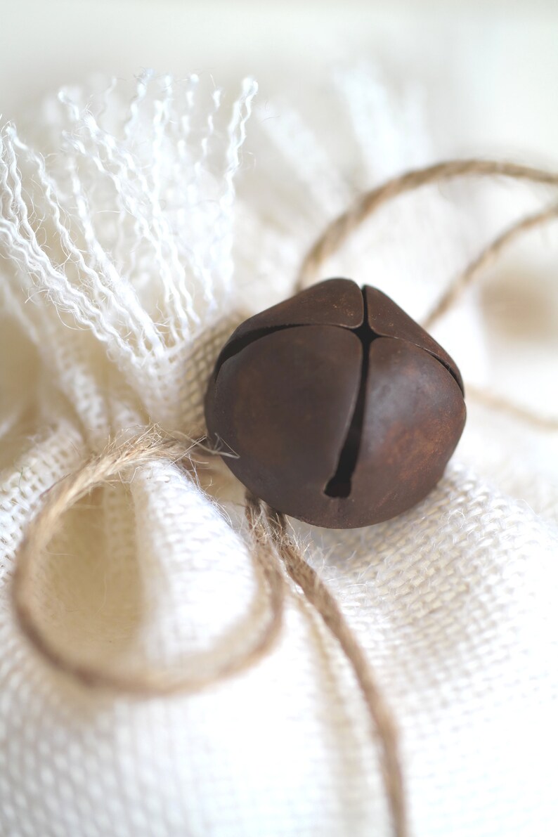May include: A rustic brown metal bell tied with twine to a white burlap bag.