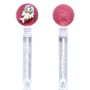 Op de afbeelding: Bellenblazers met een zeemeerminontwerp. De voorkant van de toverstaf heeft een roze cirkel met een zeemeerminfiguur, terwijl de achterkant een effen roze cirkel heeft. De toverstaven zijn van helder plastic met een bellenblaasmechanisme.