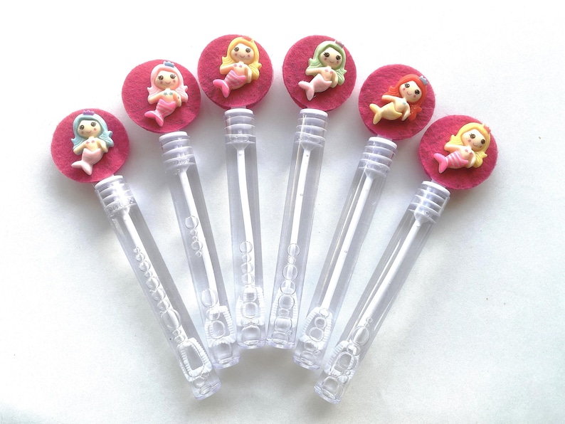 Op de afbeelding: Bellenstokken met zeemeermin-toppers. Elke toverstaf heeft een doorzichtige plastic buis met een bellenoplossing en een decoratieve bovenkant. De toppers zijn roze vilten cirkels met een zeemeerminfiguur in verschillende kleuren.