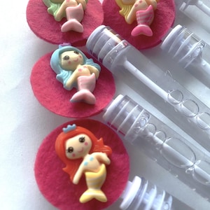 Op de afbeelding: Bellenblaasstokken met zeemeermintthema. Elke toverstaf heeft een kleurrijk zeemeerminfiguur op een roze vilten cirkel. De zeemeerminnen hebben verschillende haarkleuren en worden gecombineerd met doorzichtige plastic bellenblaasstokbuizen.