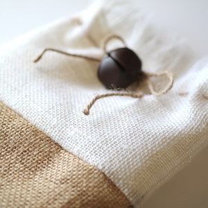 May include: A white and brown fabric gift bag with a brown jingle bell tied to the top.