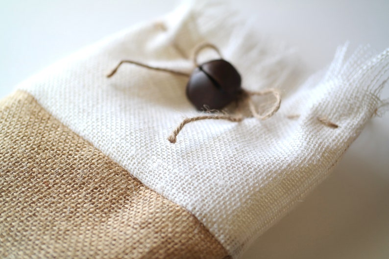 May include: A white and brown fabric gift bag with a brown jingle bell tied to the top.