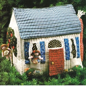 May include: A quilted dollhouse with a blue and white gingham roof, red door, and windows with blue and white patterned curtains. Two dolls are peeking out of the windows.