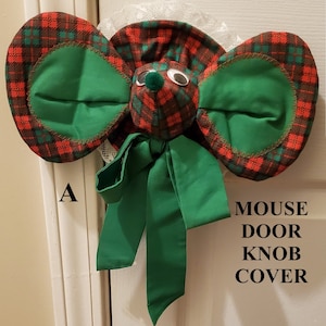 May include: A green and red plaid mouse door knob cover with a green bow. The text "MOUSE DOOR KNOB COVER" is printed on the white door.