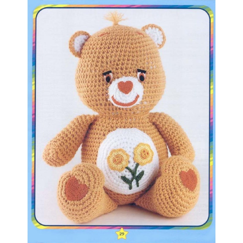 May include: A crocheted Care Bear plush toy with a yellow flower design on its belly. The bear is sitting with its arms crossed and has a heart-shaped nose.