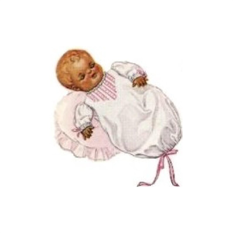 May include: A sleeping baby doll wearing a white gown with pink trim and a pink ribbon. The doll is lying on a pink pillow with ruffled edges.