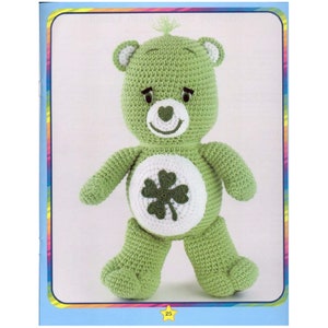 May include: Green crocheted Care Bear with a four-leaf clover on its belly. The bear has a white face with a heart-shaped nose and black eyes.